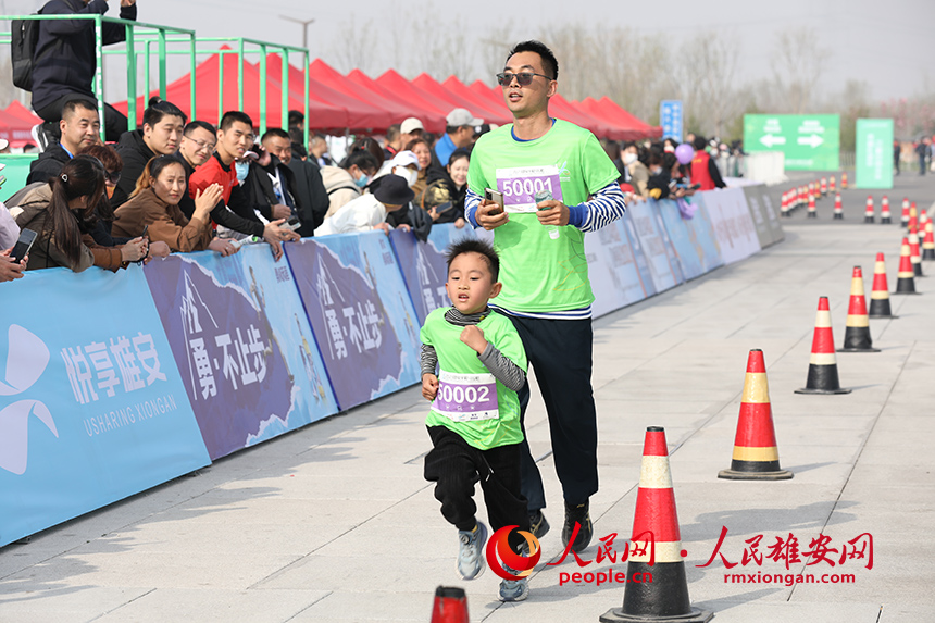 2023雄安半程馬拉鬆現場，父親帶著兒子參加家庭夢想跑。人民網 李兆民攝
