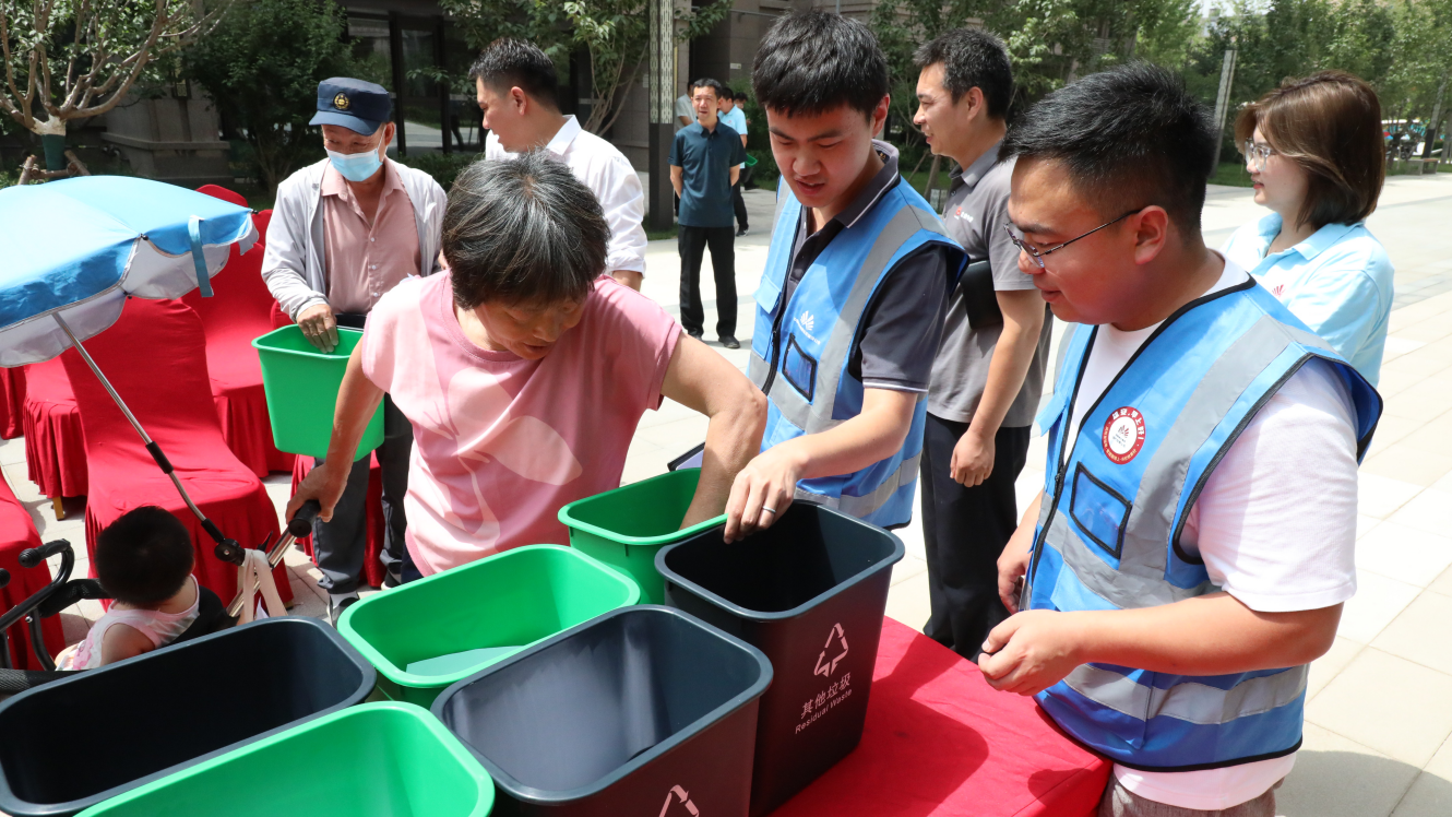 “垃圾分类志愿服务队”队员向居民发放垃圾桶。生态建设公司供图